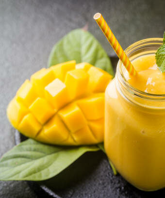 Refreshing and healthy mango smoothie in a glass with fresh fruit over stone background with copy space